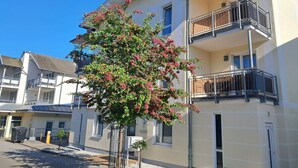 Een meerhoog gebouw met balkons, een boom met roze bloemen en een helderblauwe lucht.