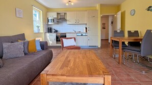 Een gezellig, compacte leefruimte met een bank, een houten tafel, een keuken met kastjes en een eettafel met stoelen.