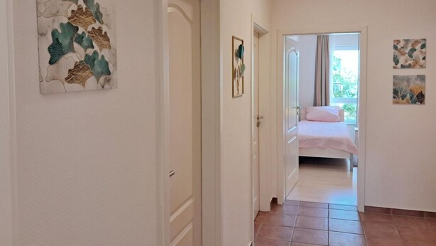 Een gang die leidt naar een slaapkamer met een bed, een deur en kunstwerken aan de muren.