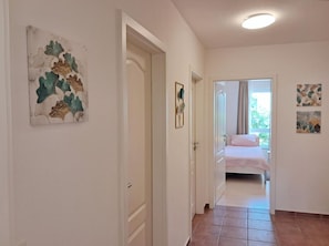 A hallway leading to a bedroom with a bed, a door, and artwork on the walls. - Central but quiet, balcony, free swimming pool and sauna - Villa Elisenhof Elli 5 (Göhren)