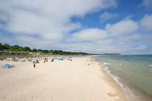 A wide sandy beach with tents and beachgoers, a clear sky, and a calm sea. - Central but quiet, balcony, free swimming pool and sauna - Villa Elisenhof Elli 5 (Göhren)