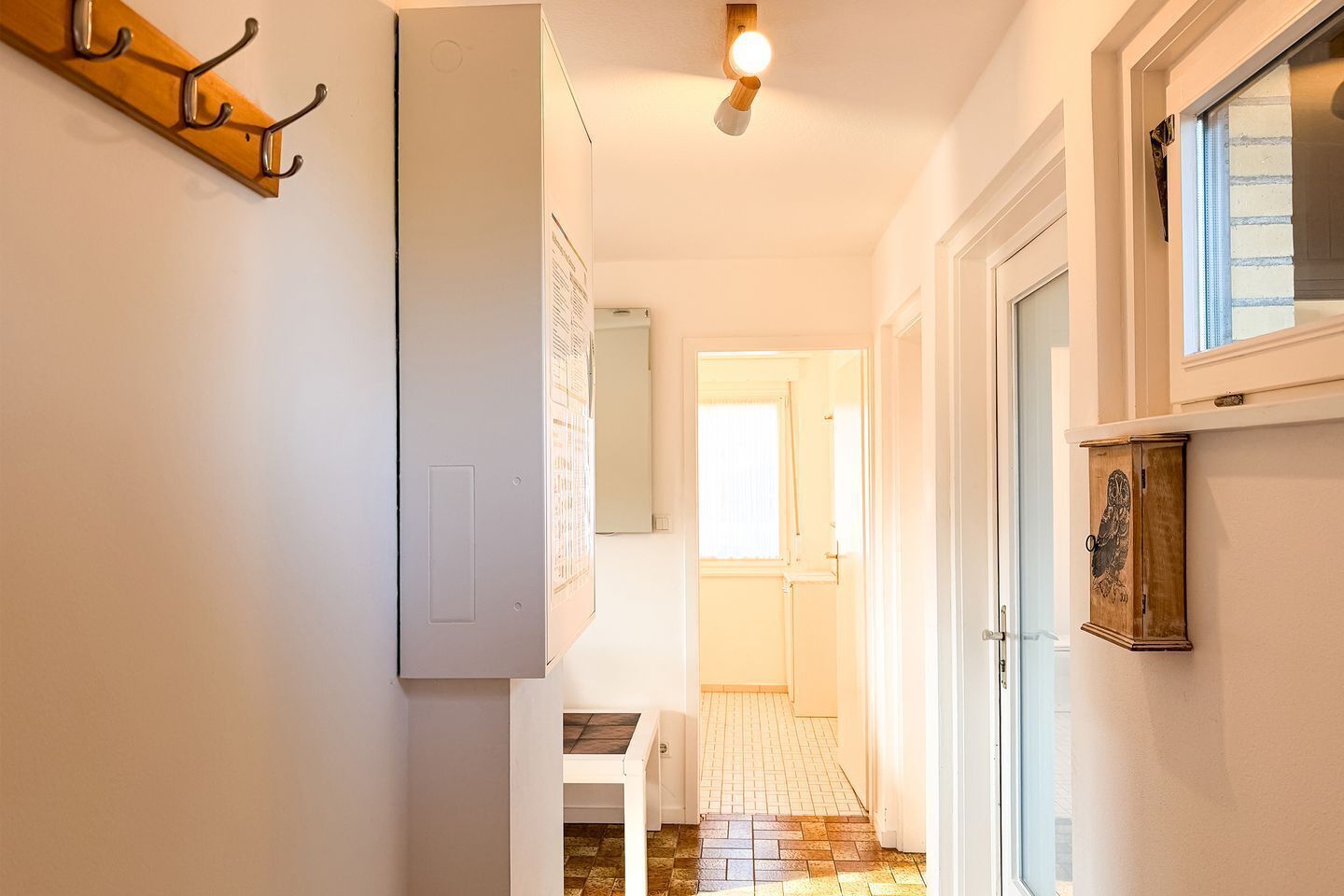 Um corredor com um cabide, um armário de madeira com decoração de coruja e uma porta que dá para outro cômodo.