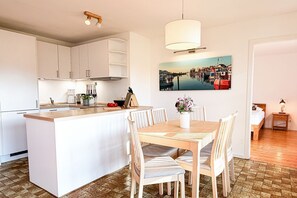 A modern kitchen with white cabinetry, a central island, and a dining area with striped chairs. - (ULM1) Jürgens Lieblingsplatz Niendorf - Holiday home "Jürgens Lieblingsplatz (Timmendorfer Strand)