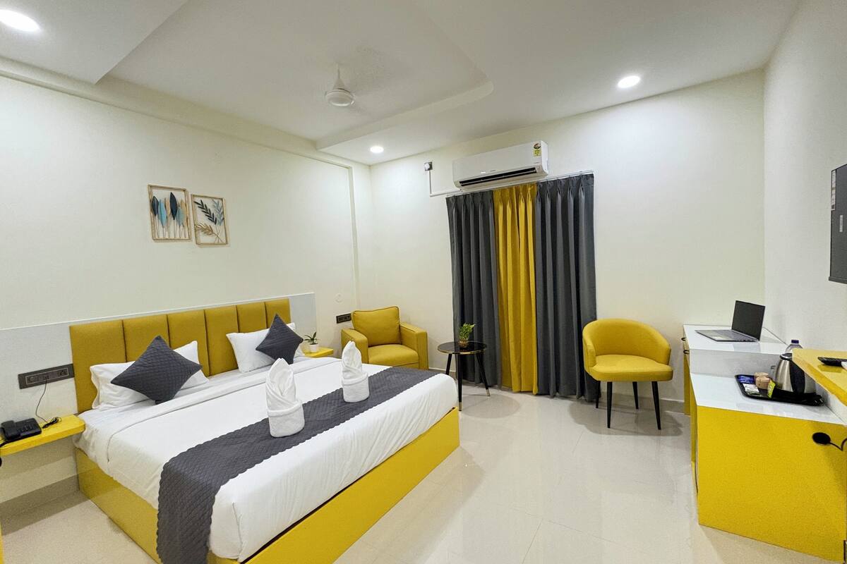 A hotel room with a bed, a desk, a chair, an air conditioning unit, and a television.