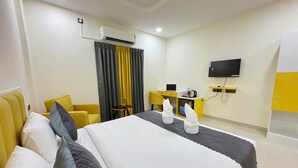 A hotel room with a bed, a desk, a chair, a TV, and an air conditioning unit. - Yellow Sapphire Hotel DLF Cyber City (Hyderabad)