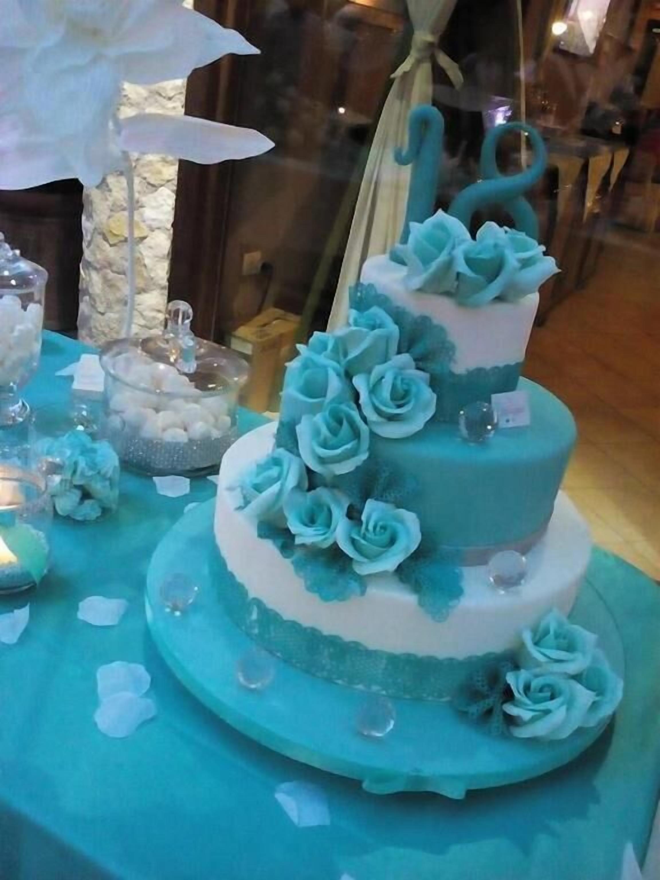 Una torta a due piani con glassa blu e bianca e decorazioni di rose.