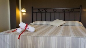 Cama bem arrumada com roupa de cama listrada, um travesseiro e uma toalha enrolada com fita vermelha.