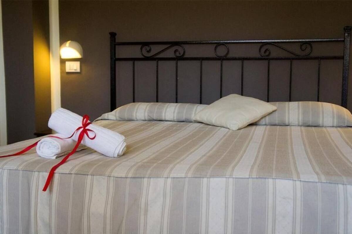 A neatly made bed with striped bedding, a pillow, and a rolled towel with a red ribbon.