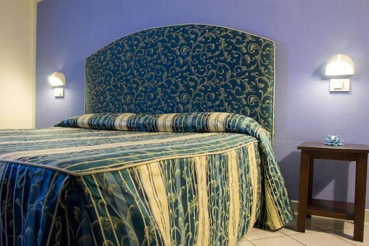 A bedroom with a large bed, two wall-mounted lights, and a small table.