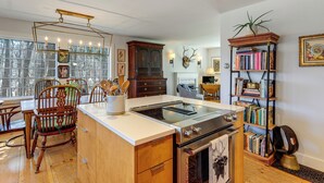 Una cocina con una isla central, sillas de madera, estufa y una estantería.