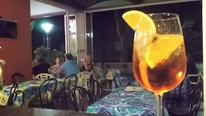 Une table sur laquelle se trouve un verre contenant une boisson, décoré d’une tranche d’orange, et autour de laquelle sont disposées des chaises recouvertes d’une nappe à motifs.