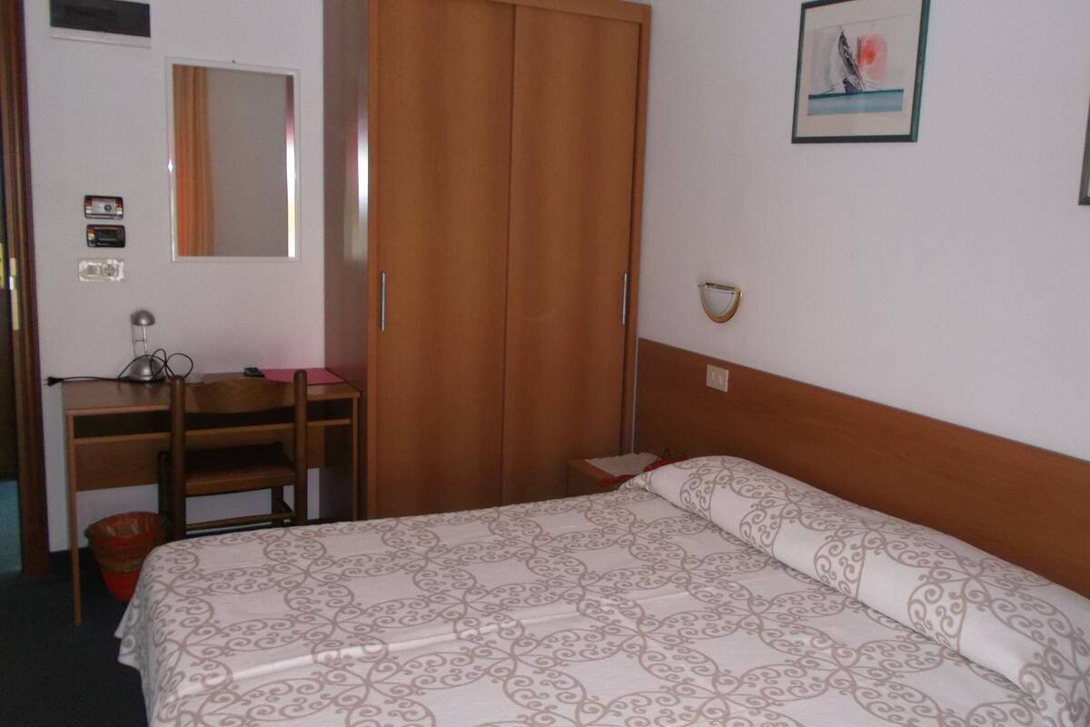 Une chambre à coucher comprenant un lit, un bureau, une armoire, un miroir et deux tableaux encadrés accrochés au mur.