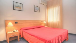 Une chambre d’hôtel avec un lit, deux lampes de chevet, une table de chevet et deux tableaux encadrés au mur.