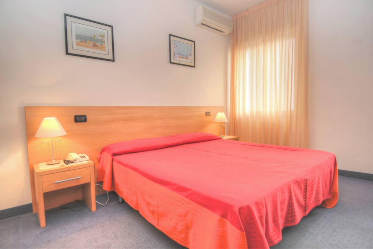 Une chambre d’hôtel avec un lit, deux lampes de chevet, une table de chevet et deux tableaux encadrés au mur.