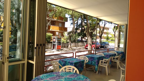 Un espace extérieur aménagé avec des tables et des chaises, donnant sur des voitures garées, et avec un bâtiment en arrière-plan.
