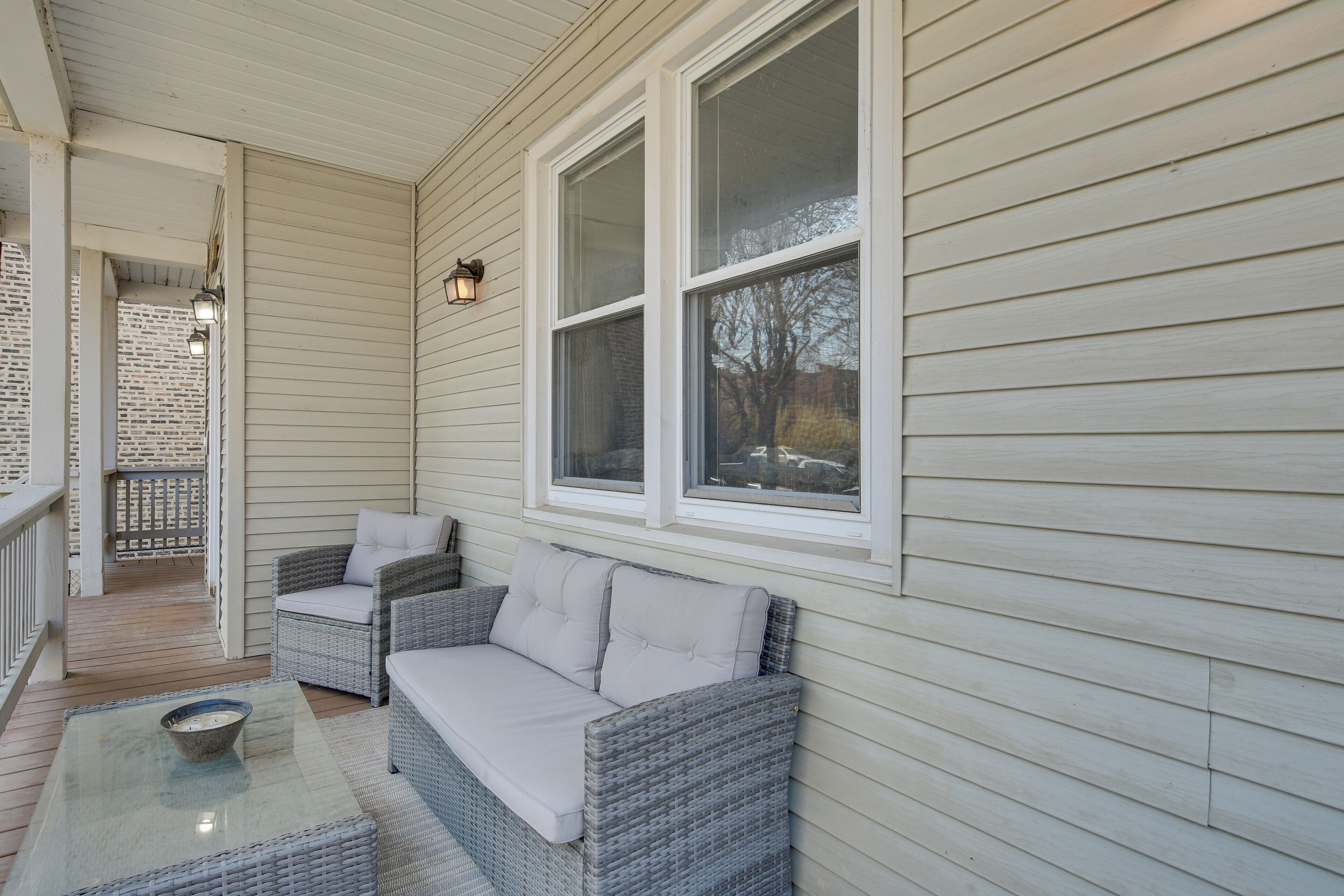A covered porch with wicker furniture, a glass table, and a view of the outside.