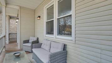 A covered porch with wicker furniture, a glass table, and a view of the outside.