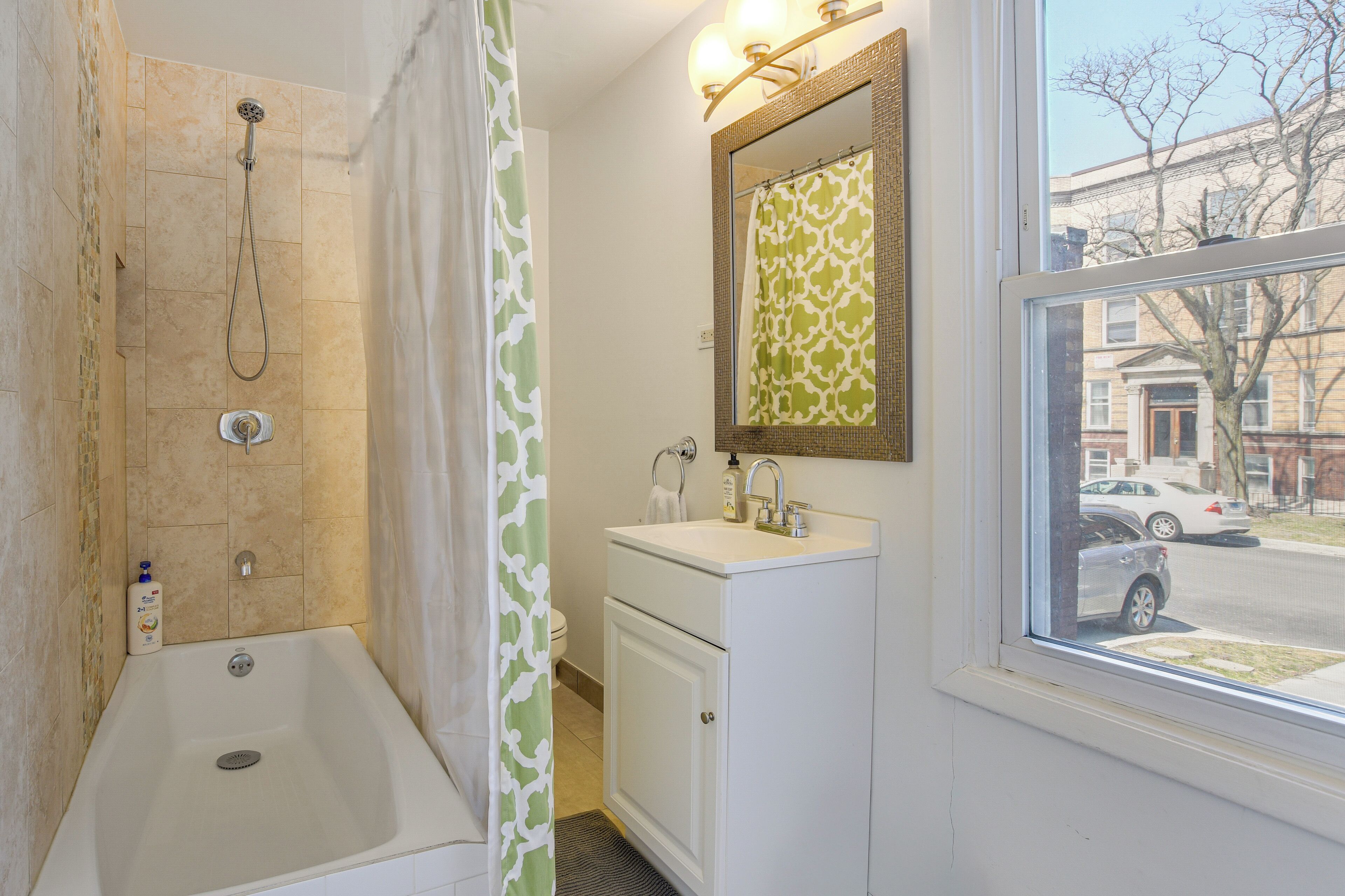 A bathroom with a shower, a sink, a mirror, and a window.
