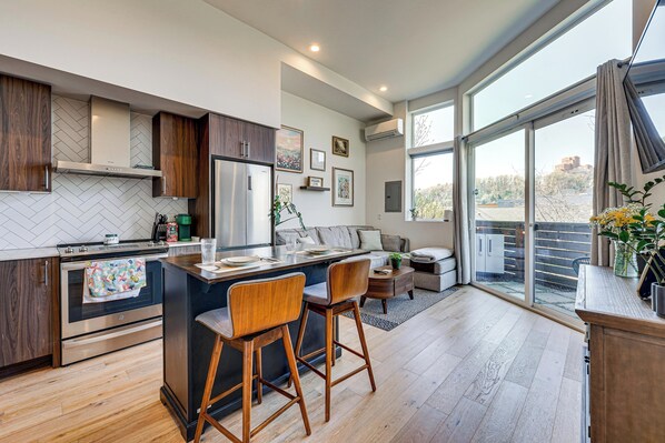 A modern kitchen with a central island, wooden bar stools, a built-in oven, and a large window offering a view of the outdoors. - Rooftop Retreat w/ City Views: Modern Seattle Home (Seattle)