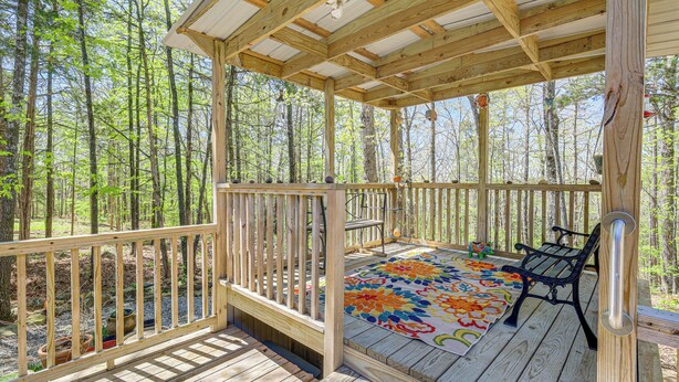Una terraza de madera con un banco y un tapete colorido, rodeada de un bosque.