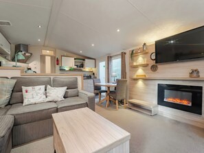 Ein modernes Wohnzimmer mit Sofa, Couchtisch, Kamin, Wandfernseher und einer Küche im Hintergrund.