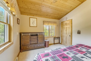 Un dormitorio con techo de madera, una cama grande con colcha, un aparador, una ventana y una puerta.