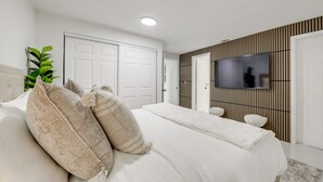 Een slaapkamer met een bed, kussens, een televisie en een plant.