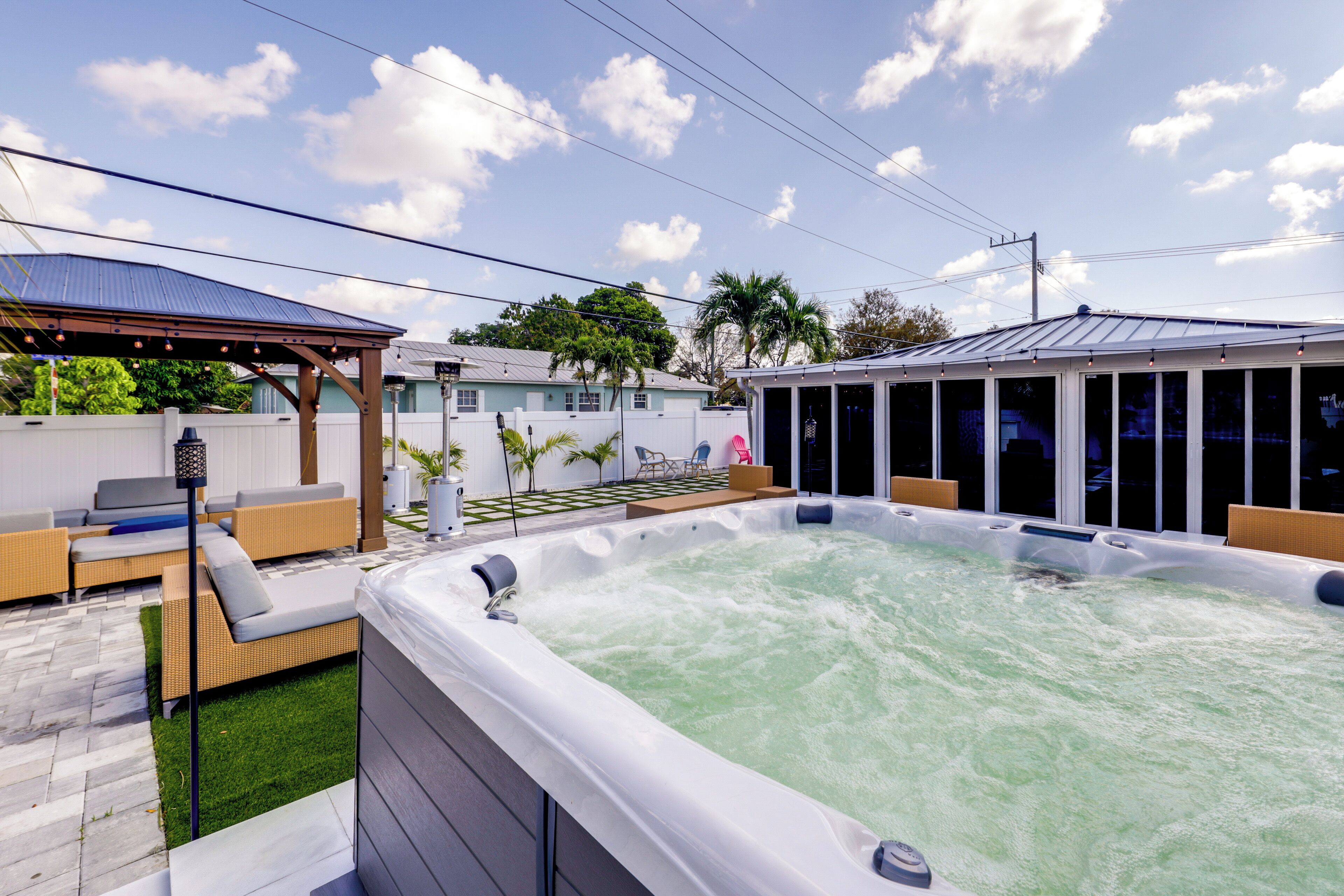 A hot tub in a backyard with a covered seating area and a house in the background.