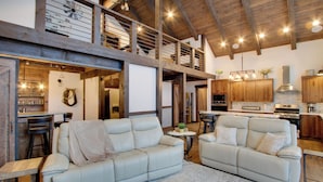 A spacious living area with two white leather sofas, a wooden ceiling, and a kitchen in the background. - Game Room & Mtn Views: Large Cle Elum Lake House (Ronald)
