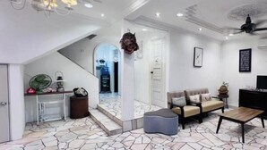 Un amplio salón con una lámpara de araña moderna, un conjunto de sofás, una mesa de centro y una escalera que lleva a otra habitación.