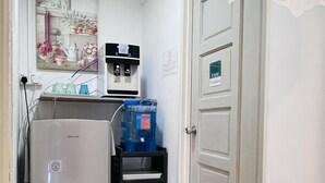 Una pequeña cocina con refrigerador, dispensador de agua y estante en la despensa.