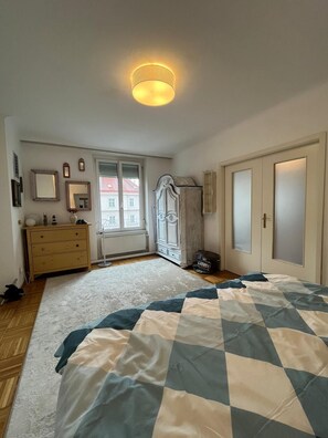 Un dormitorio con cama, cómoda, armario y ventana con contraventanas.