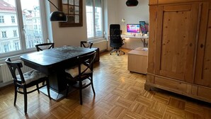 A dining area with a table and chairs, a wooden cabinet, a black office chair, a computer on a desk, and a window with a view of buildings. - 120sqm Downtown luxury flat big S-side balcony (Wien)