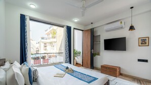 Habitación de hotel con una cama grande, televisión, aire acondicionado y balcón con vistas a edificios.