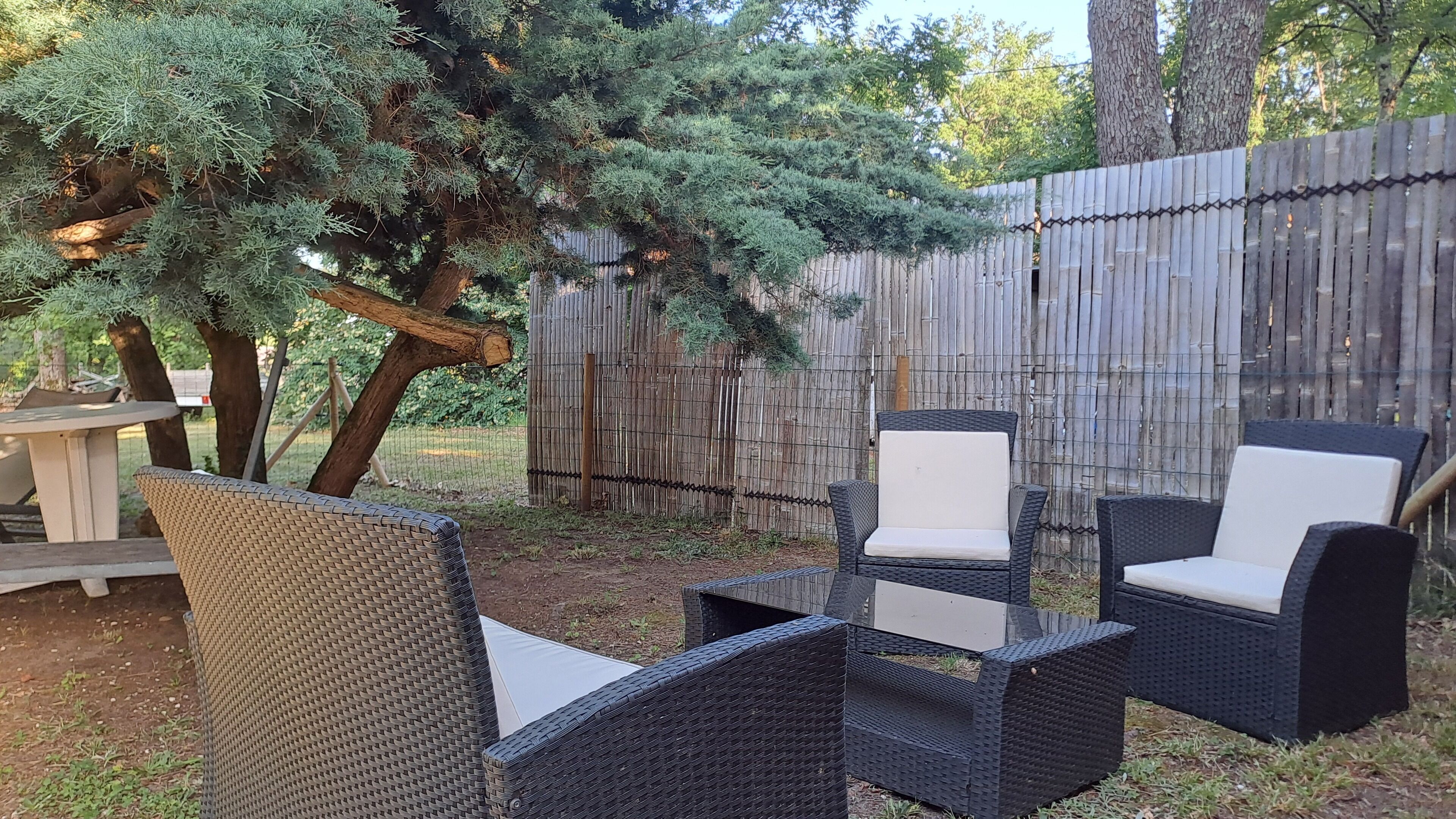 An outdoor seating area with wicker chairs and a table, surrounded by a wooden fence and trees.