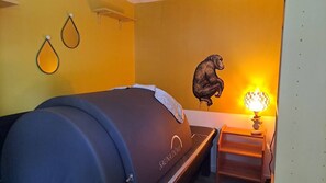 A sauna room with a large barrel, a wall-mounted heater, and a wall decoration of a gorilla.