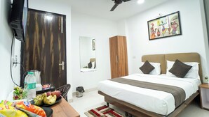 Una habitación de hotel con una cama, un ventilador de techo, un televisor montado en la pared, un armario de madera, un espejo y una pequeña mesa con aperitivos.
