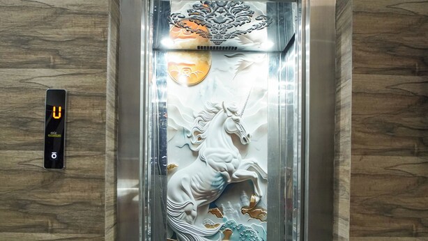 Un ascensor con un panel decorativo que muestra un jinete a caballo, una pantalla digital y un suelo con diseño de mármol.