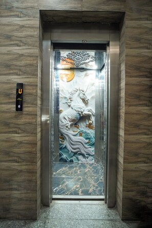 An elevator with a decorative panel featuring a horse and rider, a digital display, and a marble-patterned floor. - Hotel Aerosky Prime (New Delhi)