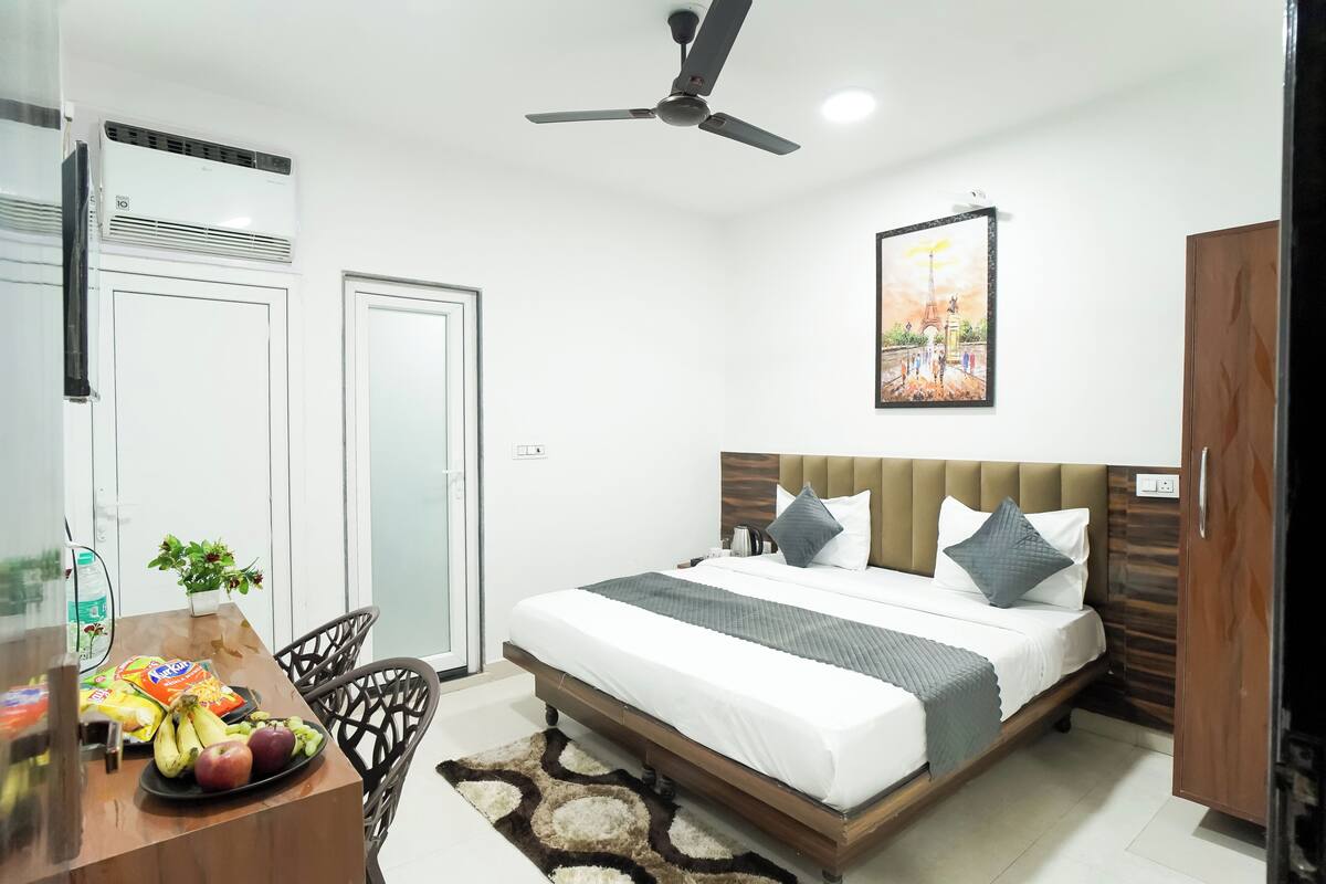 A bedroom with a bed, a ceiling fan, a painting, and a dining area with fruits and snacks.