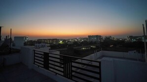 Terraza en la azotea con barandilla, con vistas a un paisaje urbano al atardecer.