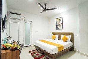 A bedroom with a bed, a ceiling fan, a wall-mounted TV, a painting, and a dining area with a table and chairs. - Hotel Aerosky Prime (New Delhi)