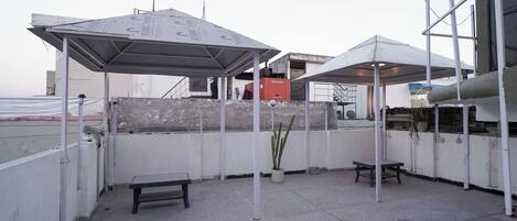 Una terraza en la azotea con dos zonas de estar cubiertas, una planta en maceta y una caja roja.