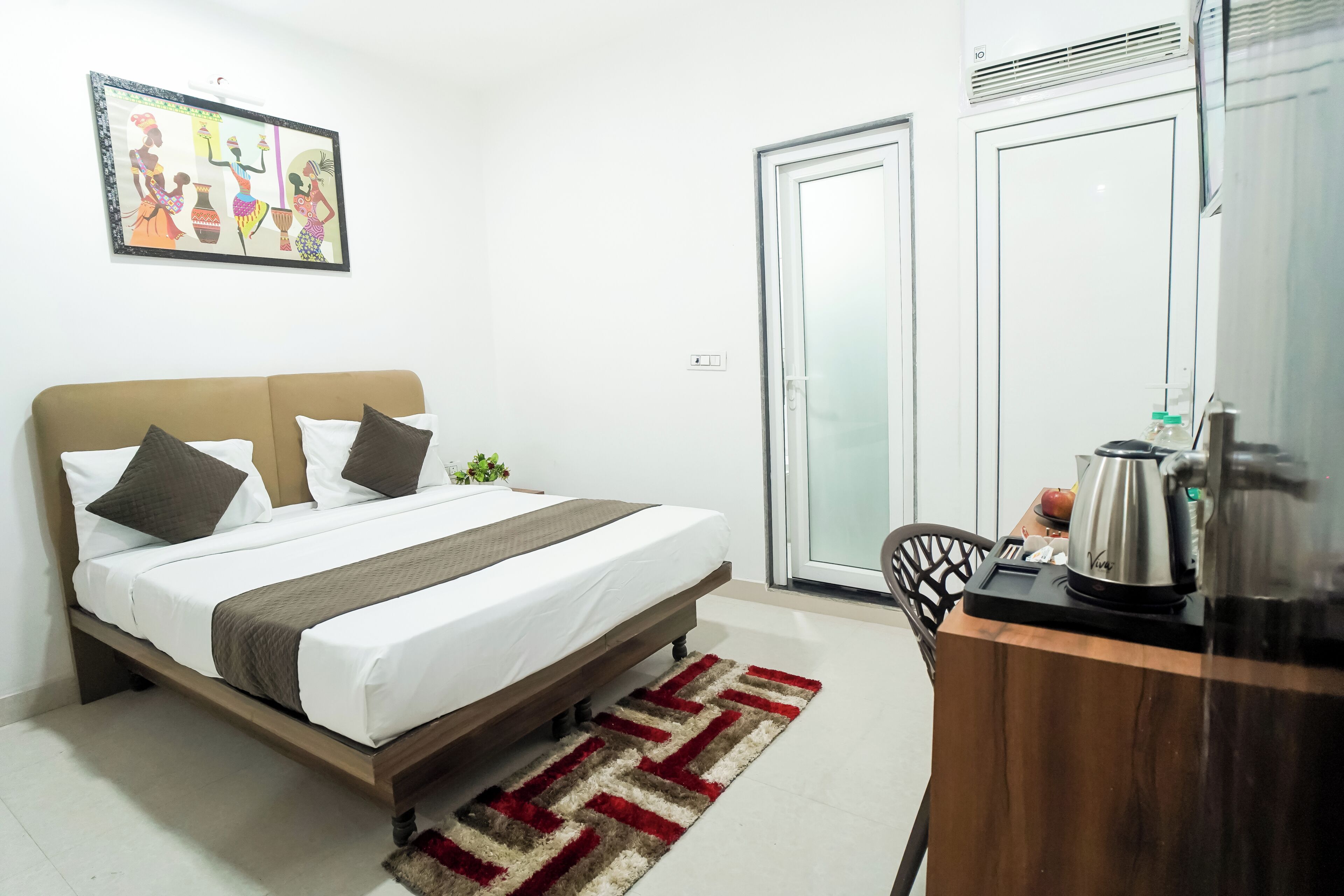 A bedroom with a bed, a desk with a kettle, and a door.