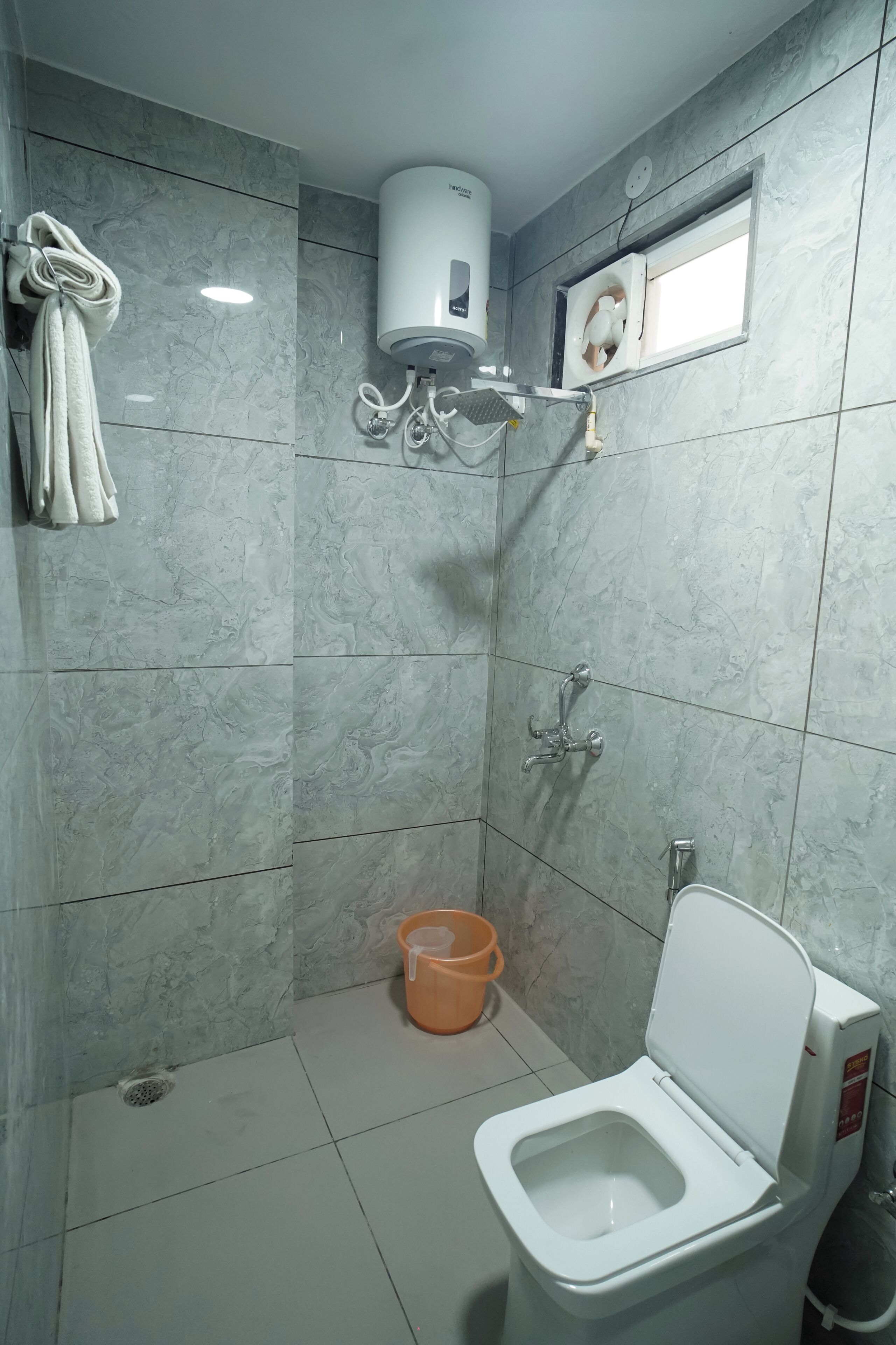 A bathroom with a toilet, a shower, a towel rack, and a window.