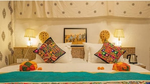 A hotel room with a bed, two nightstands, two lamps, a framed picture, and a decorative wall hanging. - Desert Cactus Resort Jasialmer (Sam)