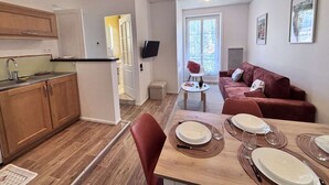 A compact living space with a kitchenette, a dining area, a red sofa, and a TV mounted on the wall. - Adria - 1 bedroom - Near the Thermal Park (Châtel-Guyon)