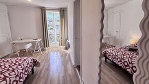 A hotel room with a mirrored wall, a dining table with chairs, a bed with patterned bedding, and a view through a window with curtains. - Adria - 1 bedroom - Near the Thermal Park (Châtel-Guyon)