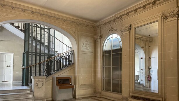 A grand hallway with a marble floor, a staircase with a wrought iron railing, and a large arched window. - Adria - 1 bedroom - Near the Thermal Park (Châtel-Guyon)