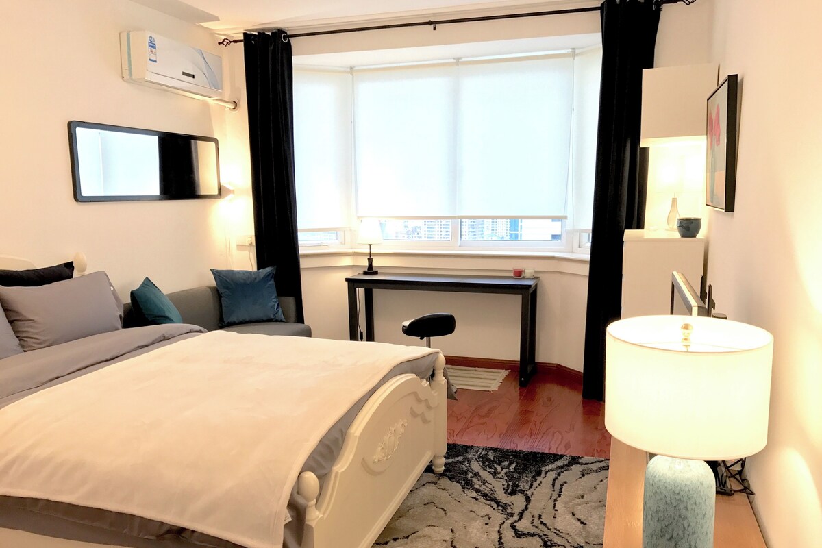 Een hotelkamer met een bed, bureau, stoel, lamp en een raam met uitzicht.